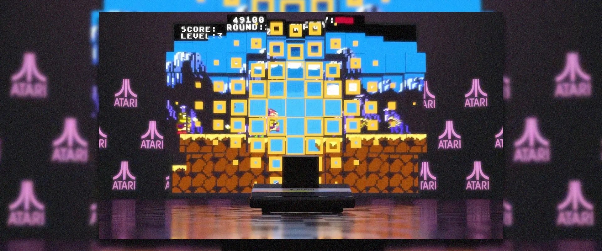 Imagem do Atari 7800 com imagem de um jogo ao fundo e logos da Atari aos lados